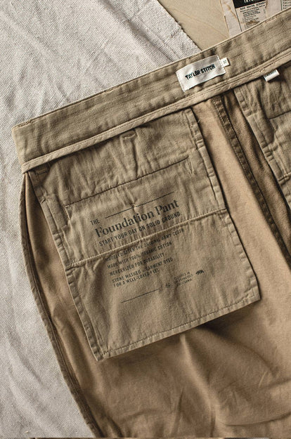 A pair of Foundation Pants folded on a black background, showing the back pocket.